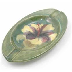 A Moorcroft Hibiscus oval ashtray, post war, decorated with a single flowerhead against a green g...