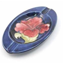 A Moorcroft Hibiscus oval ashtray, post war, decorated in shades of pink and green, against a blu...