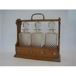 AN EDWARDIAN OAK TANTALUS, nickel mounts, containing three fluted clear glass decanters/stoppers,...