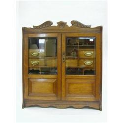 AN EDWARDIAN OAK SMOKERS CABINET, twin bevelled glazed doors opening to an arrangement of drawers...