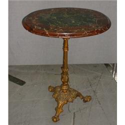 Un guéridon ovale, le plateau de marbre bicolore sur un support tripode en fonte dorée....