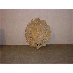 Un blason héraldique en bronze patiné dans un encadrement de feuilles de chêne....