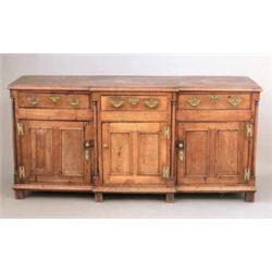 A George III oak breakfront dresser base, with three frieze drawers over three panelled doors, wi...