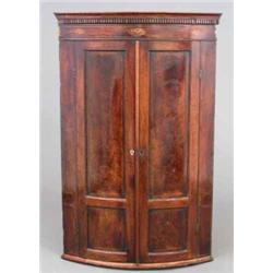 A George III inlaid mahogany bowfront hanging corner cupboard, with two panelled doors enclosing...