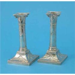 A pair of Edwardian silver candlesticks with ionic column stems and loaded swept square bases, 19...