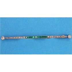 A gold bar brooch, set calibre-cut emeralds flanked by round cut diamonds with diamond terminals...