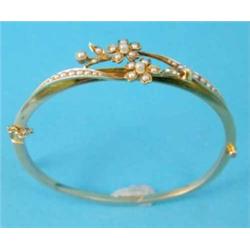 A gold hinged bangle, the front designed as two sprays of flowers set split pearls...