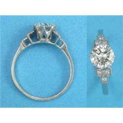 A platinum solitaire diamond ring, the claw-set brilliant cut stone flanked by diamond set steppe...