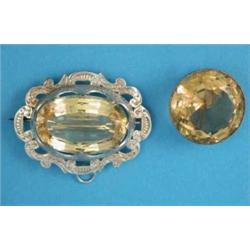 A circular citrine brooch, in plain gold frame and an oval citrine brooch in engraved silver scro...