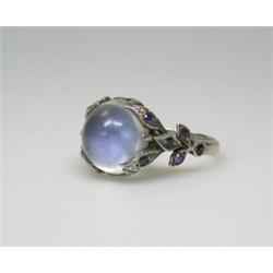 A white metal moonstone ring mounted with a spherical stone above foliate shoulders set with tiny s.