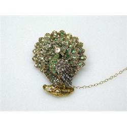 A gold brooch modelled as a peacock with tail feathers displayed, decorated with emeralds and rose..