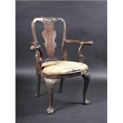 An early 18th century walnut open armchair, the carved arched top rail above a solid vase shaped sp.