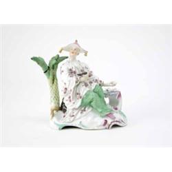 A Hochst figure of a Chinaman shown seated on a rocky base with scrolling edge, a tree on one sid...