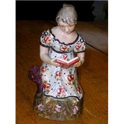 A late 18th century pearlware figure of a girl wearing a floral dress and seated by a tree trunk re.