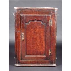 A George III oak hanging corner cupboard, the moulded cornice above an arch panelled door enclosing.