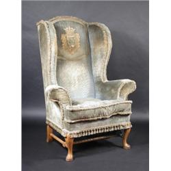 An 18th century style wing back armchair, the arched padded back with embroidered armorial between..