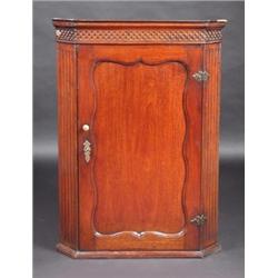 A George III mahogany hanging corner cupboard, the moulded cornice with blind fretworked frieze abo.