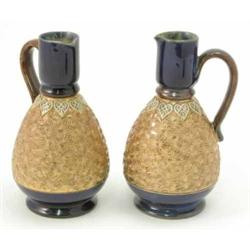 A pair of Royal Doulton glazed stoneware ewers, with ovoid bodies gilded and moulded with flowers...