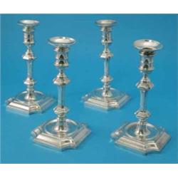 A set of four George V silver candlesticks, the double baluster faceted stems supported on shaped...