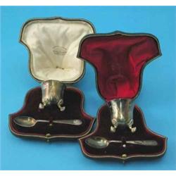A pair of cased Edwardian silver egg cups and spoons, with scroll feet, makers Goldsmiths & Silve...