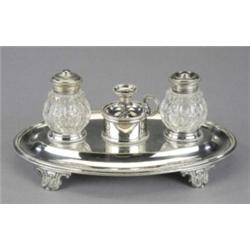An oval inkstand, with beaded borders and leaf scroll feet, fitted two ovoid cut glass wells with...