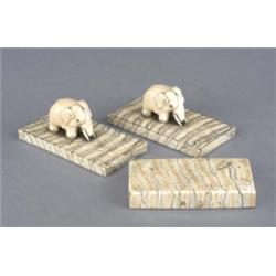 A pair of paperweights, the rectangular fossilised mammoth tusk bases supporting carved ivory ele...
