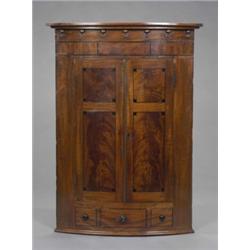 A post-Regency figured mahogany bow-front hanging corner cupboard, the two shelves enclosed by a...