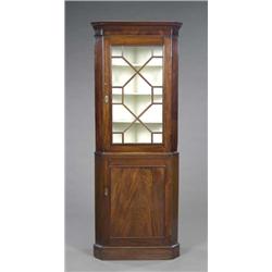 A George IV mahogany standing corner cabinet, composed, the three shaped shelves enclosed by a la...