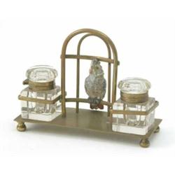A Victorian brass inkwell stand, with a model of a caged parrot between a pair of cut glass inkwe...
