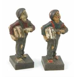 Two 'Spheshul' cold painted figures of an urchin newspaper seller, one with green, the other with...