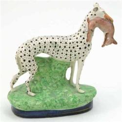 A Victorian Staffordshire greyhound, painted with black spots, holding dead hare in jaw, on mould...