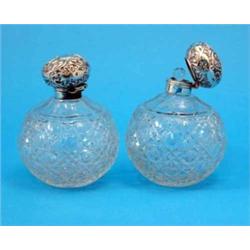 A pair of Edwardian silver topped cut glass globular scent bottles, and stoppers, with foliate de...