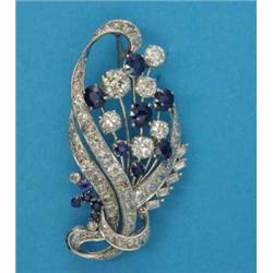 A platinum sapphire and diamond brooch, designed as a stylised ribbon tied floral spray, set oval...