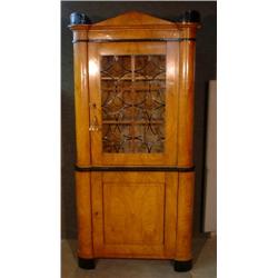 Une vitrine d'angle Biedermeier en noyer et bois noirci, vers 1830, le fronton triangulaire flanq...