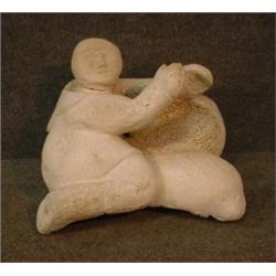 Un sujet inuit en os de baleine sculpté représentant un personnage assis près d'un masque....