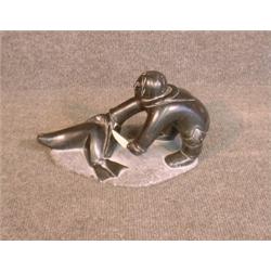 Une sculpture inuit en stéatite représentant un chasseur dépeçant un phoque....