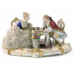 A large Dresden figure group, female in lace dress, and male companion, seated at table playing c...