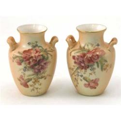 A pair of Royal Worcester two-handled vases, painted with flowers against a blush ivory ground, d...