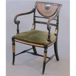 A Regency ebonised and parcel gilt elbow chair, with crescent caned back and scroll arms on spira...