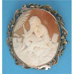 A Victorian shell cameo brooch, carved with a study of a seated putti scribe, in gold scrolled fr...