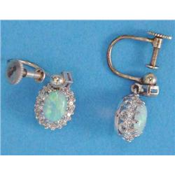 A pair of opal and diamond drop earrings, each claw-set in white gold with an oval opal in a bord...