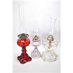 Three pressed glass oil lamps including two colourless including one turning purple and a ruby glass