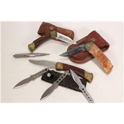 Three pocket knives, two with leather pouches, a set of three throwing knives and a metal spike.