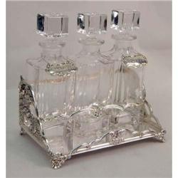 A VERY ORNATE SILVER PLATED FOOTED TANTALUS WITH THREE DECANTERS