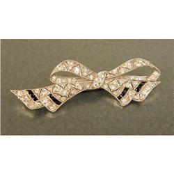 A PLATINUM, DIAMOND AND BLACK ONYX BOW BROOCH