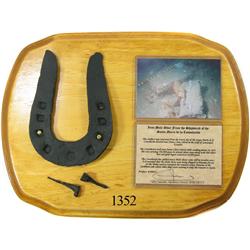 Conserved iron mule shoe and nails mounted on wooden display plaque.