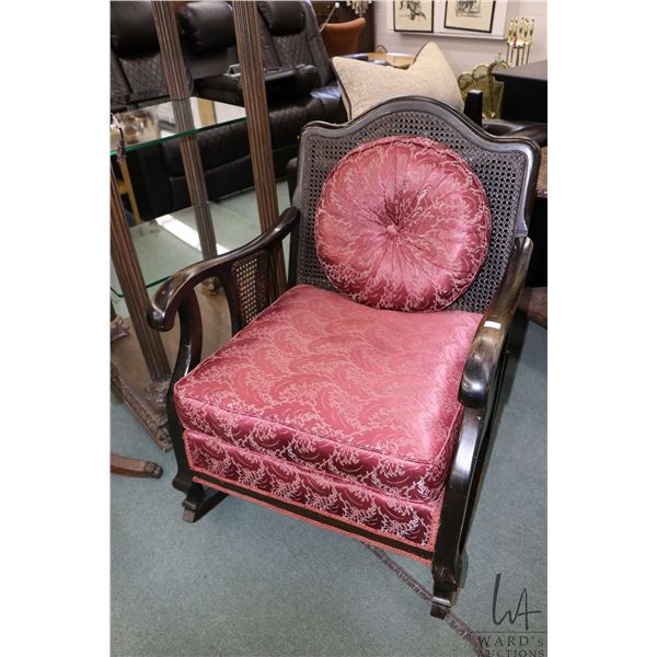 Antique rocking chair with caned back and cushioned seat, includes matching throw cushion