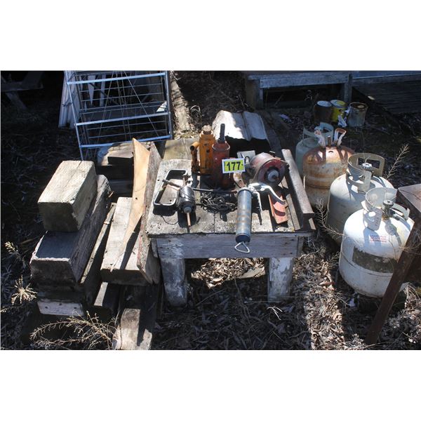 Misc. bottles jacks, grease gun, heavy steel table with vise, steel barrel and propane tanks