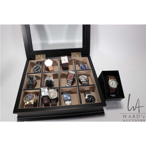 Glass topped wooden watch box containing twelve assorted men's watches plus a boxed Roots watch, all