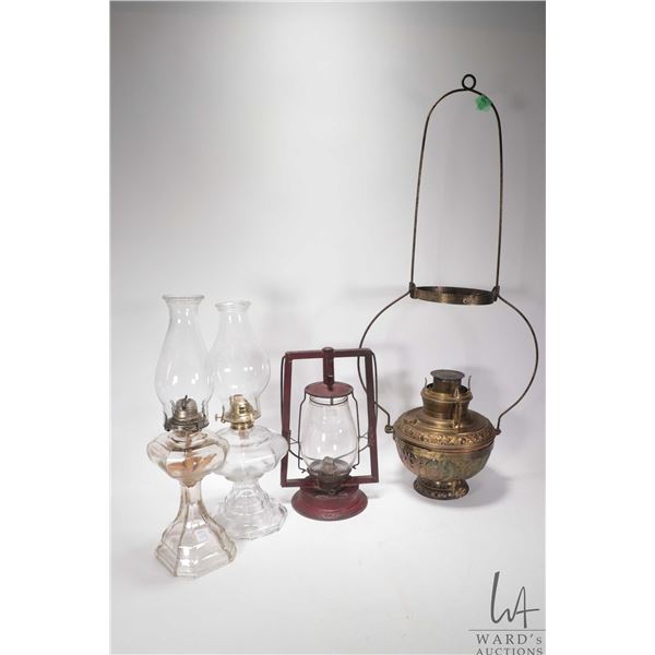 Four antique oil lamps including two colourless glass with chimneys, red barn lamp and bas relief br